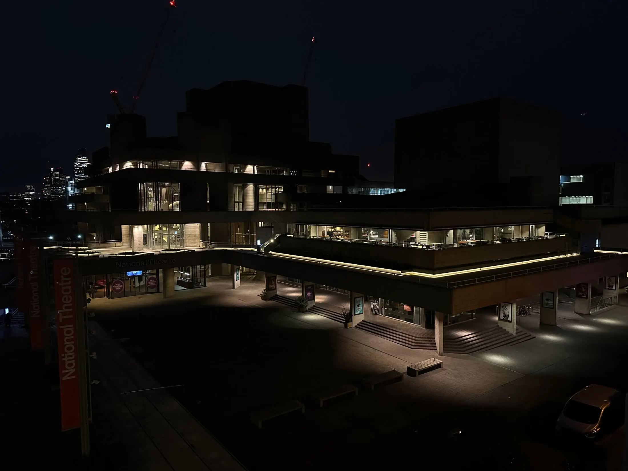 The National Theatre before dawn, mostly in shadow with precise lines of warm light tracing the building